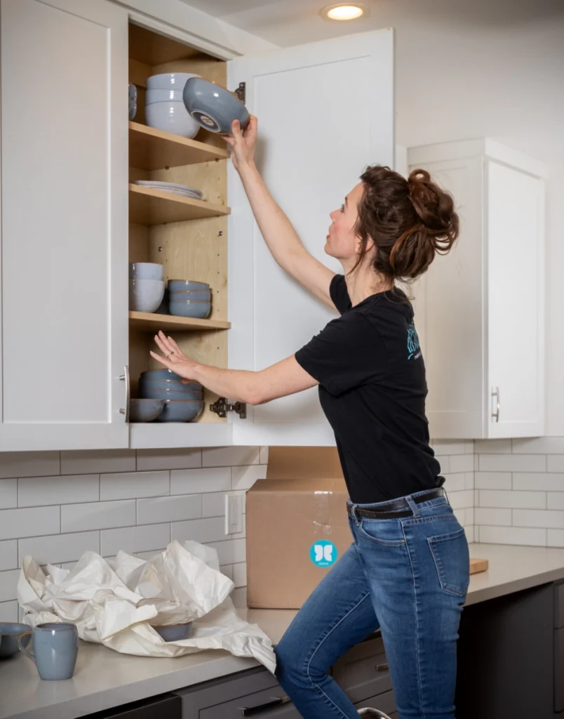 Woman unpacking and organizing dishes in kitchen cabinet.