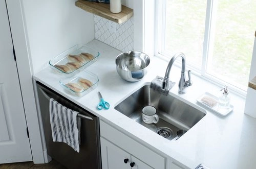 Bright and clean kitchen sink with dishes, scissors, and glass baking dishes nearby, emphasizing the topic of organizing everything under the kitchen sink.