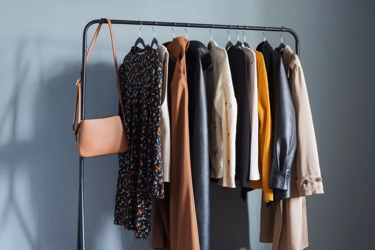 Photo of a standing clothing rack with an array of neutral color coats, dresses, and a purse hanging from it