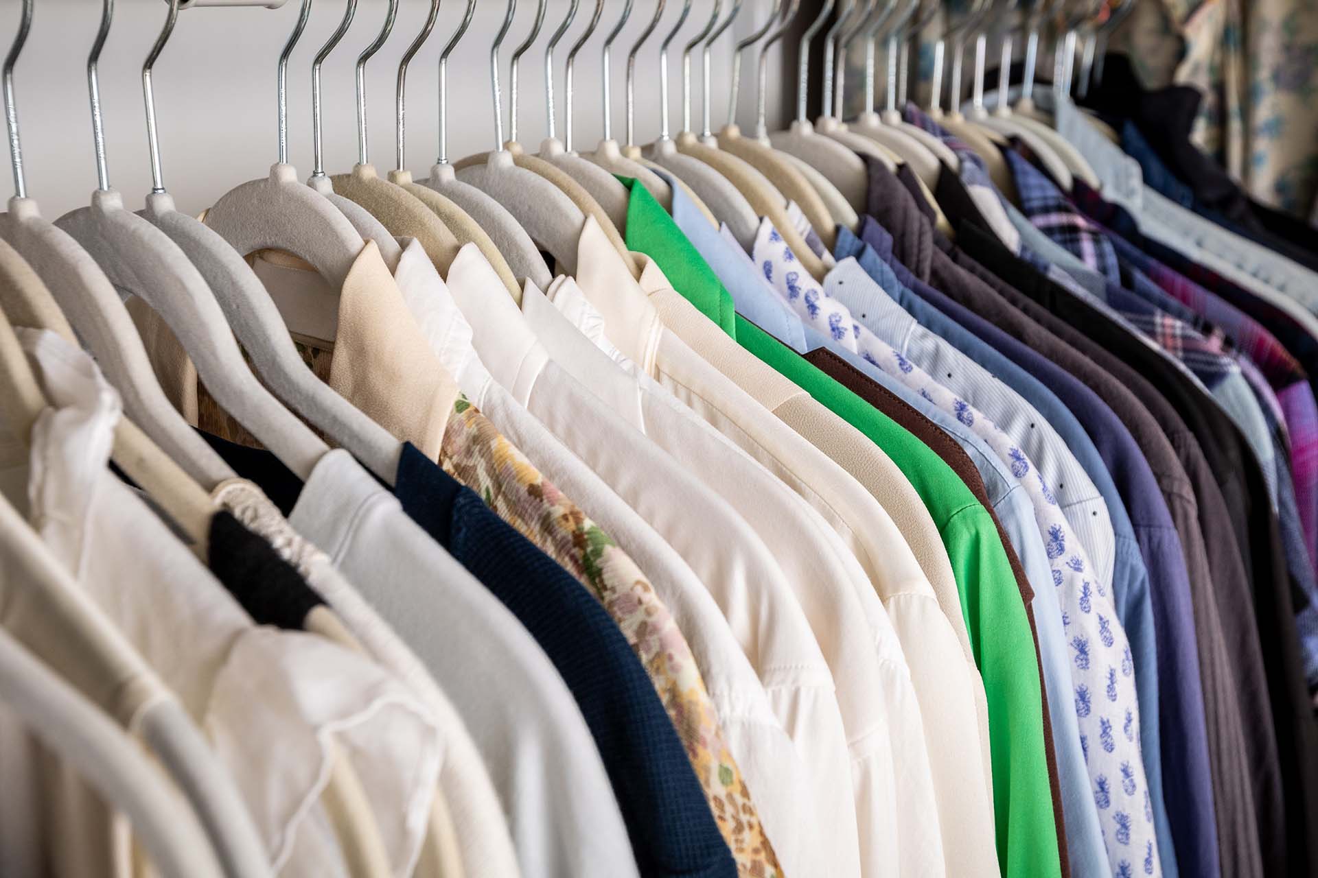 A neatly arranged wardrobe with various shirts on hangers, including white, green, and patterned designs.
